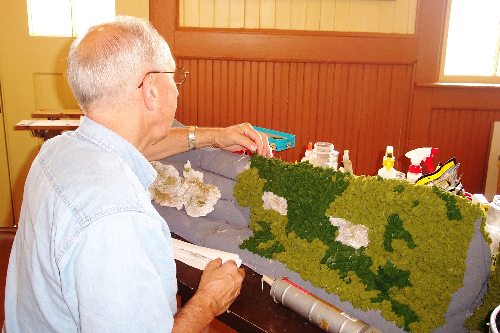 Apple Valley Model Railroad Clubs  
       member Doug Maroldi adding scenery to one of the mountains on the layout